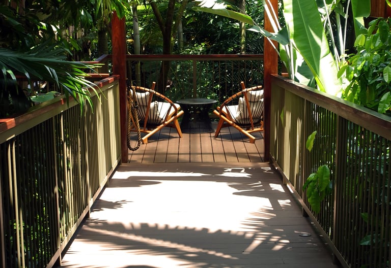 Board walkway to lounge chairs and table at a luxurious eco-resort among tropical plants