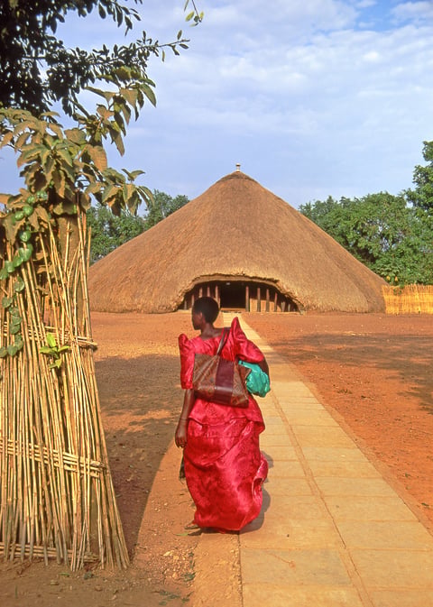 Tombs of the Buganda Kings at Kasubi, Kampala, Uganda - UNESCO World Heritage Site - woman in traditional red dress visiting a monument