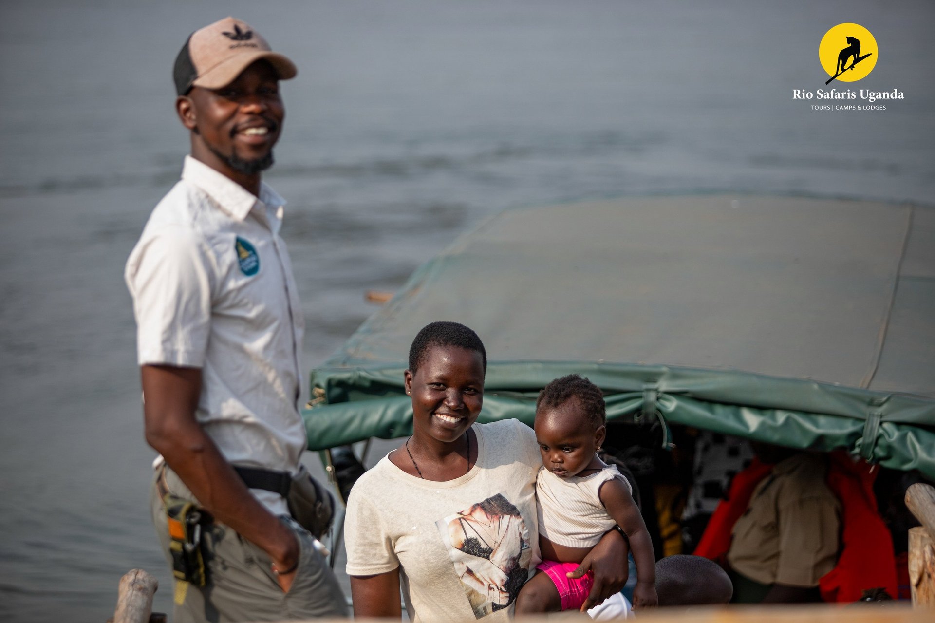 A man, woman, and young child on a boat near water, with Rin Safaris Uganda logo in the corner