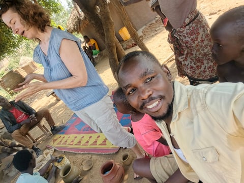 Young boy smiling at camera with woman in blue shirt during outdoor community activity in African village setting