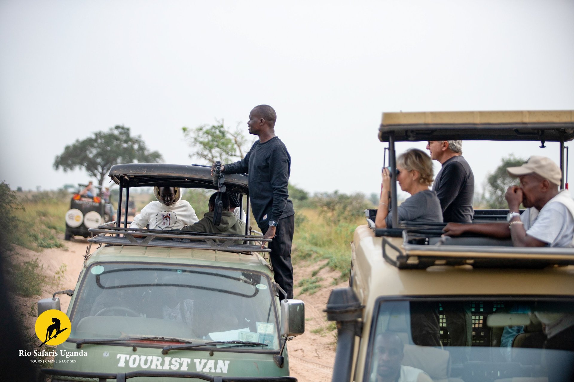 Safari guides and tourists in open-air vehicles on dusty African roadway during wildlife game drive