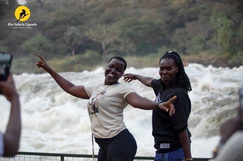Two women posing at a railing with a rushing river and forested hillside in the background