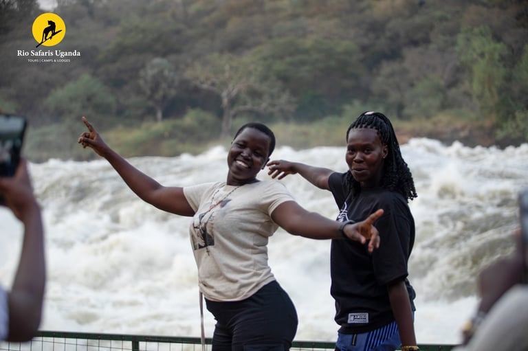 Two women posing cheerfully at a railing with a rushing river and forested hillside in the background