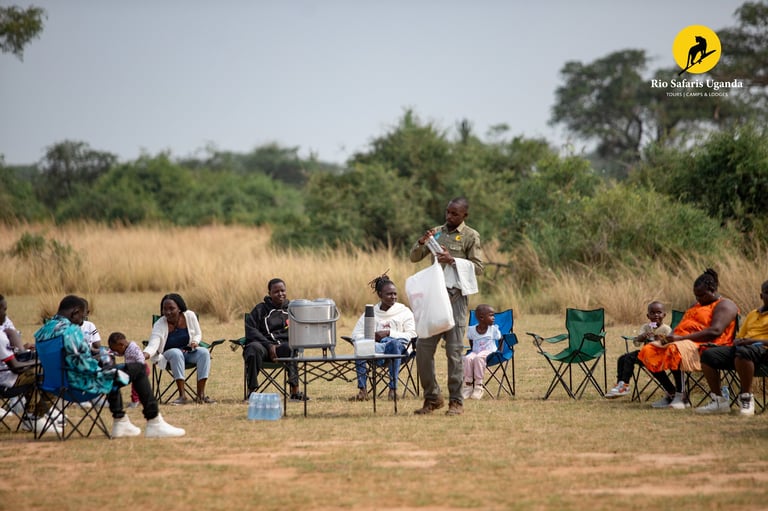Outdoor community gathering in an open field with people seated in camp chairs around a central table and speaker