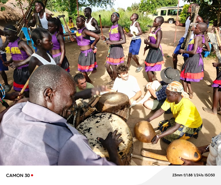 Community gathering in Cameroon where adults and children in colorful clothing participate in a traditional cooking or food preparation activity outdoors.