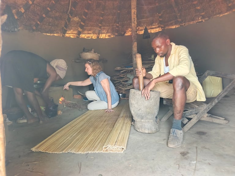 Three men inside a thatched-roof structure working with wood and traditional crafting materials on the floor