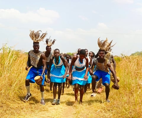 Group of dancers in blue athletic wear performing with ornate headdresses in an African savanna grassland setting