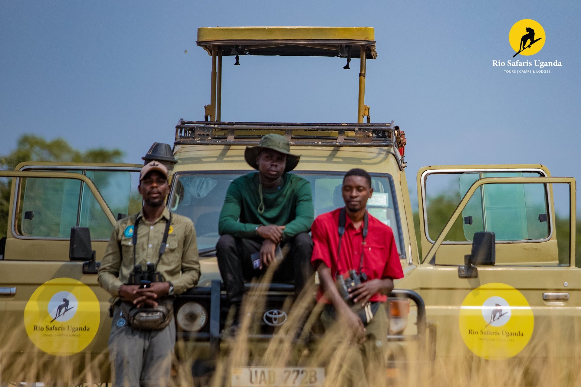 Three guides sitting on hood of safari vehicle with open roof during African wildlife tour