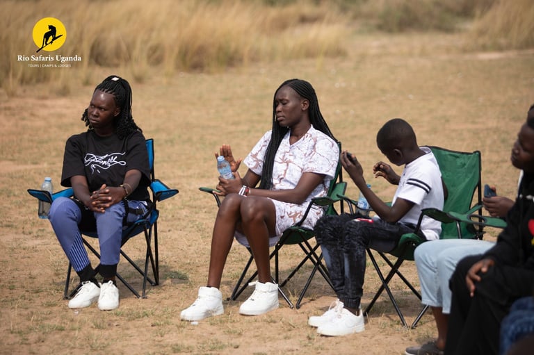 Group of young women sitting outdoors in folding chairs on sandy ground during a community gathering