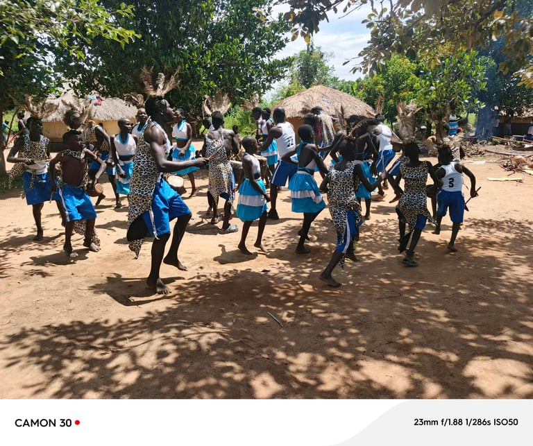 Group of school children in blue uniforms dancing and celebrating outdoors in a rural African village setting with thatched huts