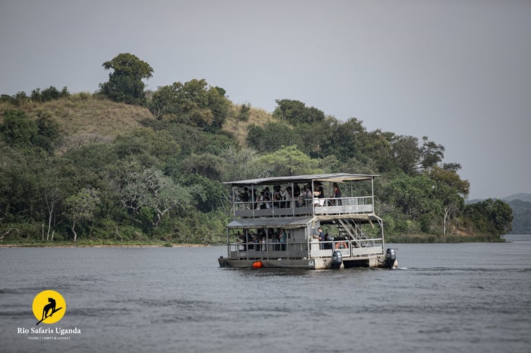 Multi-deck safari boat floating on calm water with lush green hillside and trees in the background