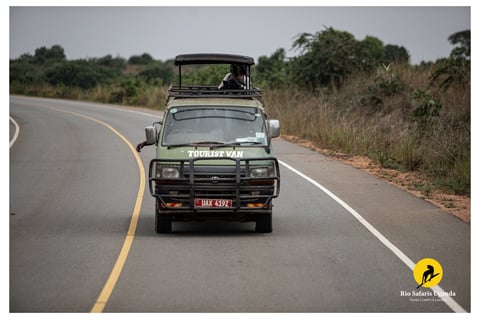 Safari jeep driving on paved road through African savanna landscape