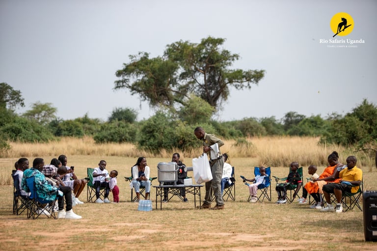 A group of people seated in a circle on folding chairs in an arid landscape with a large acacia tree in the background.