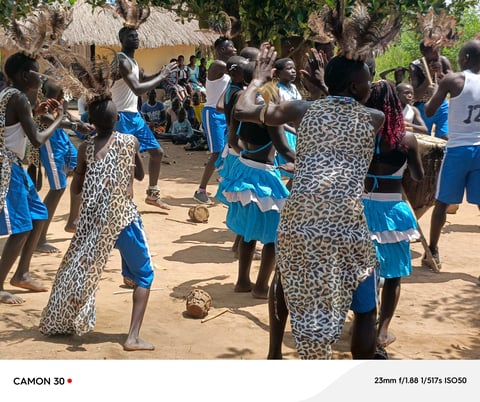 Children in blue uniforms playing and celebrating together in a village community gathering with traditional thatched buildings in background