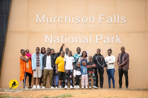 Group of diverse people standing together in front of Murchison Falls National Park mural sign