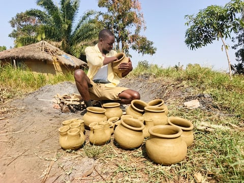 Artisan craftsman working with clay pottery vessels in a rural village setting surrounded by palm trees