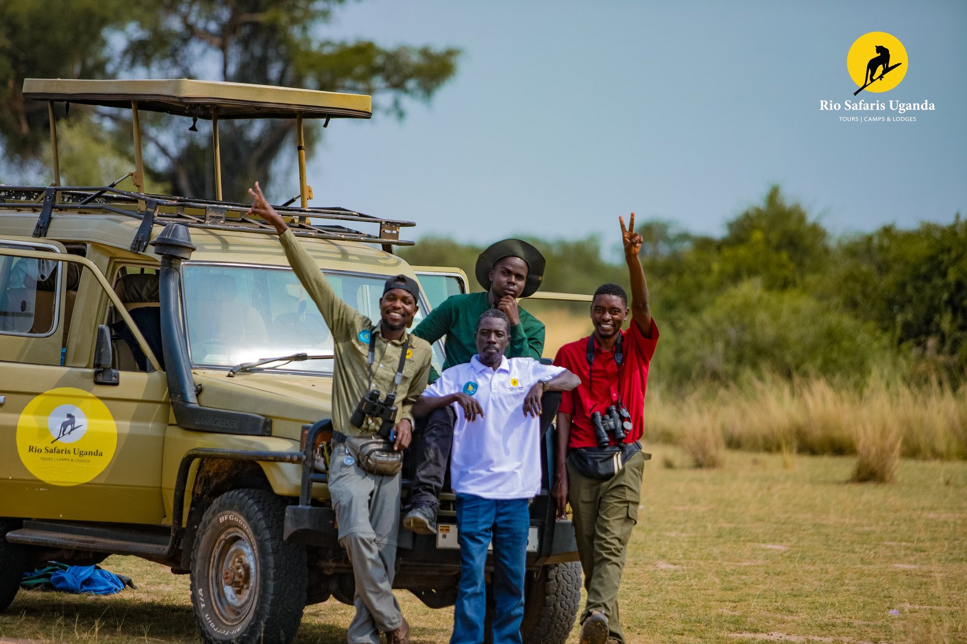 Safari guides and tourists posing happily next to a yellow safari vehicle in an African savanna landscape
