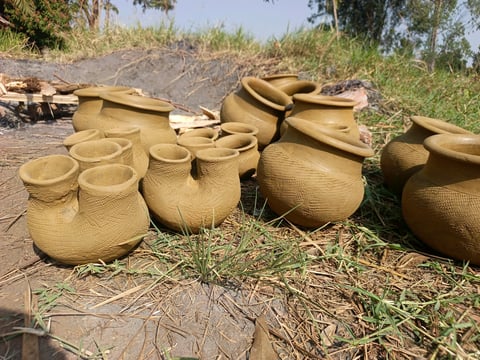 Collection of woven clay pots and baskets laid out on dried grass and soil in an outdoor setting