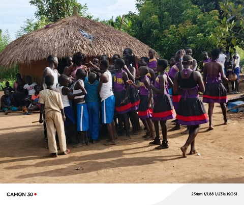 Group of people in traditional African clothing gathered outside a thatched-roof hut in a village setting