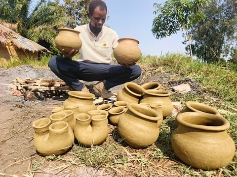 Man displaying handcrafted woven baskets and clay pots arranged on the ground outdoors